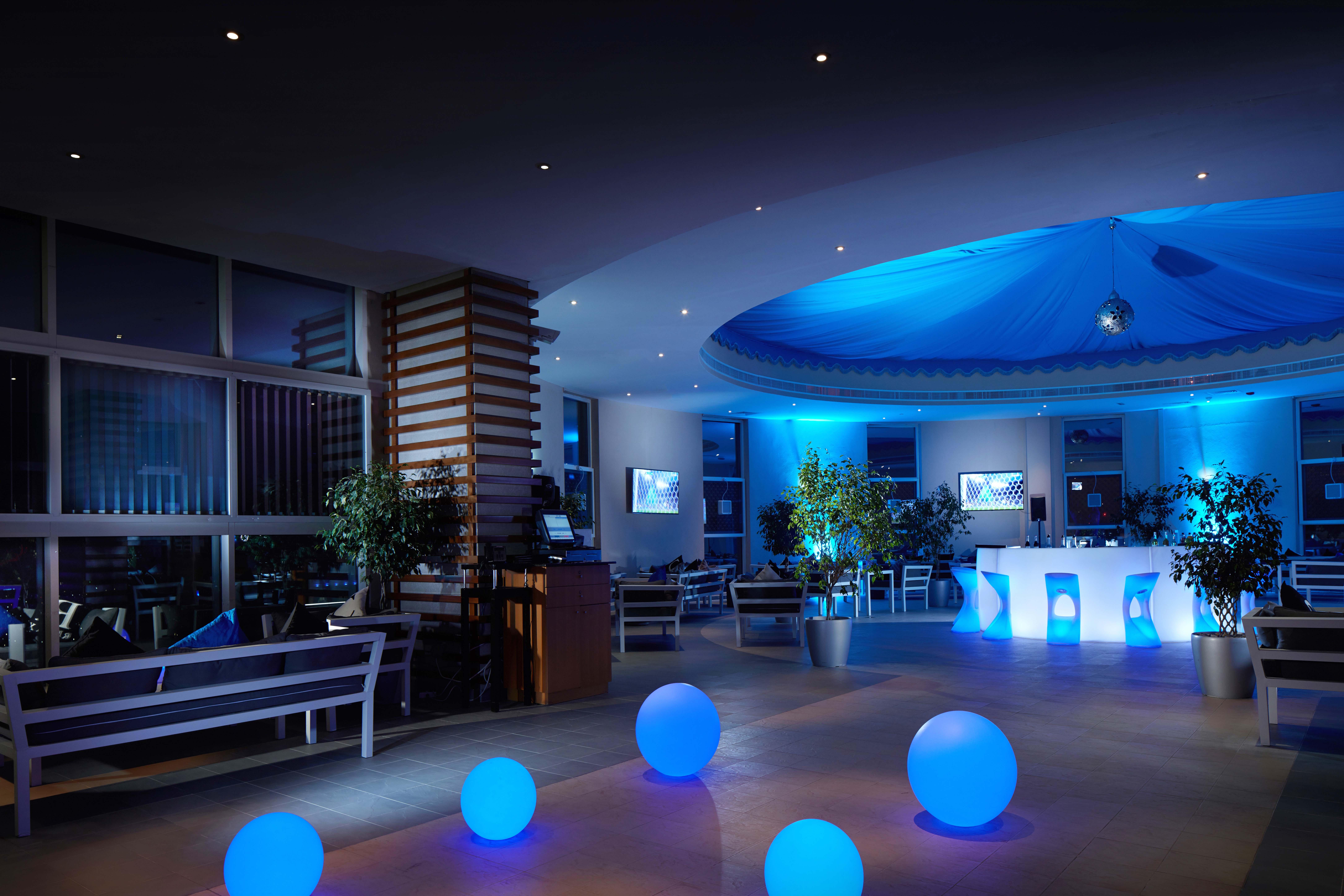 Grand Millennium Al Wahda Hotel And Executive Apartments Abu Dhabi Exterior photo The photo depicts a modern interior space, likely a lounge or reception area. The lighting is predominantly blue, creating a calm and inviting atmosphere. There are several large, glowing blue spheres placed on the floor, which add a decorative eleme