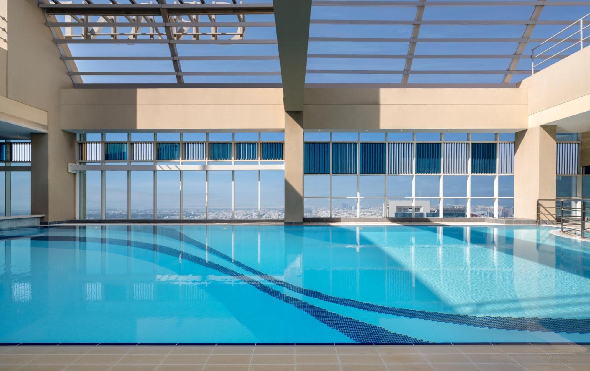 Grand Millennium Al Wahda Hotel And Executive Apartments Abu Dhabi Exterior photo The photo shows an indoor swimming pool with a clear blue water surface. The pool is surrounded by large windows that let in natural light, creating a bright and airy atmosphere. The ceiling has a grid-like structure, likely made of glass, allowing m