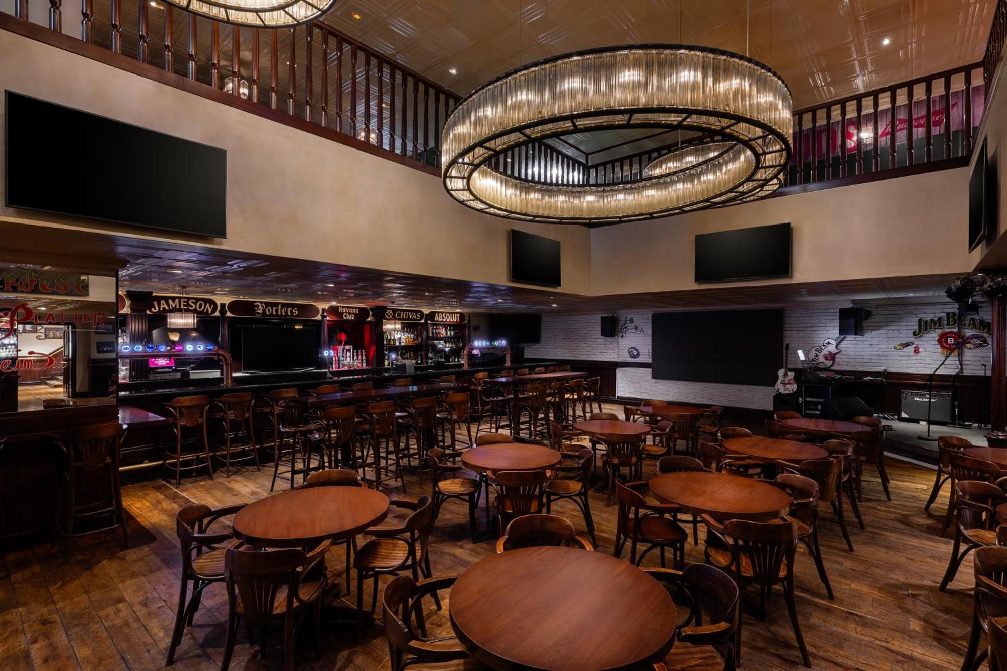Grand Millennium Al Wahda Hotel And Executive Apartments Abu Dhabi Exterior photo The photo shows the interior of a bar or pub, characterized by a spacious layout. There are several round wooden tables scattered throughout the area, accompanied by curved wooden chairs. The bar is prominently featured in the back, with shelves poss