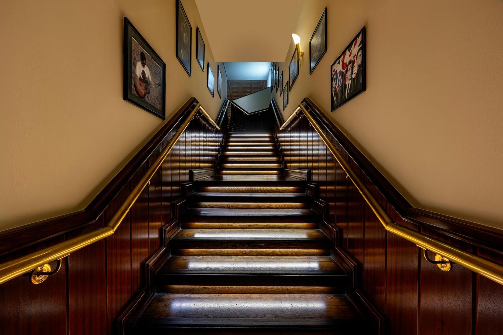 Grand Millennium Al Wahda Hotel And Executive Apartments Abu Dhabi Exterior photo The photo shows a staircase with wooden stairs and illuminated treads. The walls on either side of the staircase are adorned with framed pictures, which add decorative elements to the space. There is a warm, inviting glow from the lights along the ra