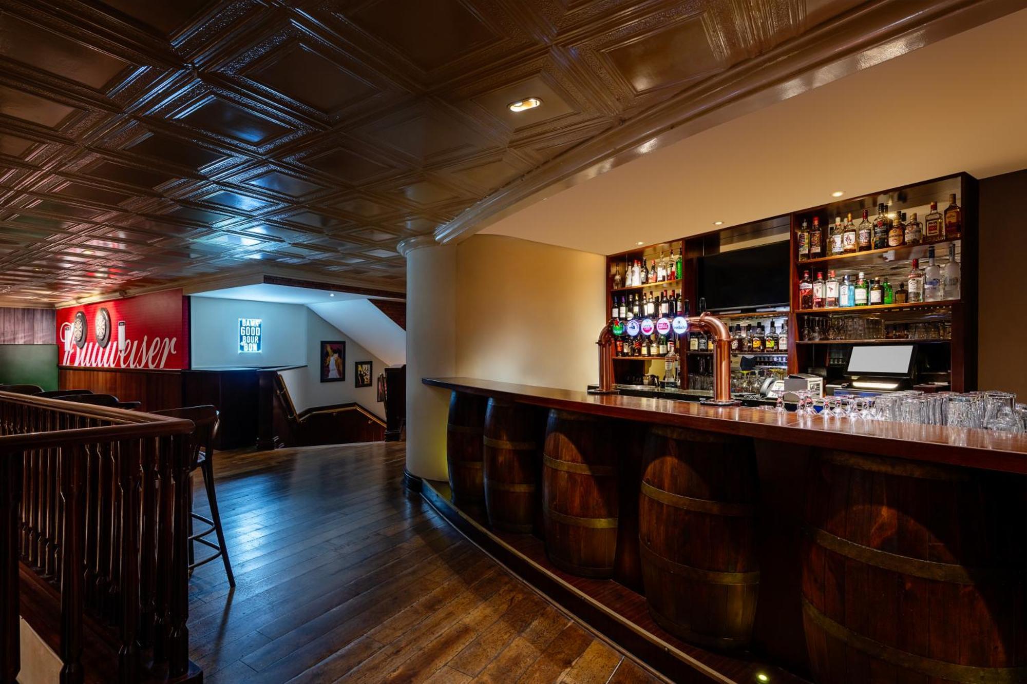 Grand Millennium Al Wahda Hotel And Executive Apartments Abu Dhabi Exterior photo The image shows an interior of a bar or pub. The space features a polished wooden bar with several barrels used as decorations. Behind the bar, there is a variety of alcoholic beverages displayed on shelves. The floor is made of dark wood, and the ce