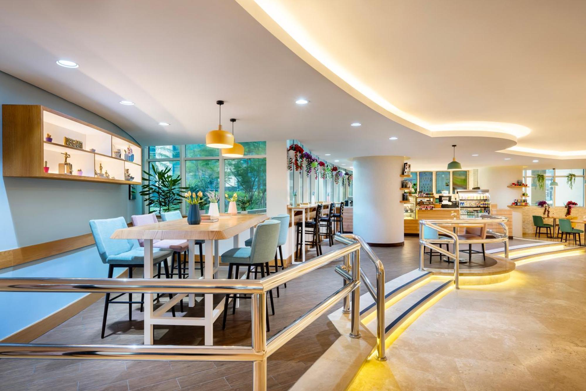Grand Millennium Al Wahda Hotel And Executive Apartments Abu Dhabi Exterior photo The photo shows a modern and stylish interior of a café or restaurant. The space is well-lit with soft, warm lighting and features a mix of seating arrangements. There are high tables accompanied by stools, and some areas have more traditional dining