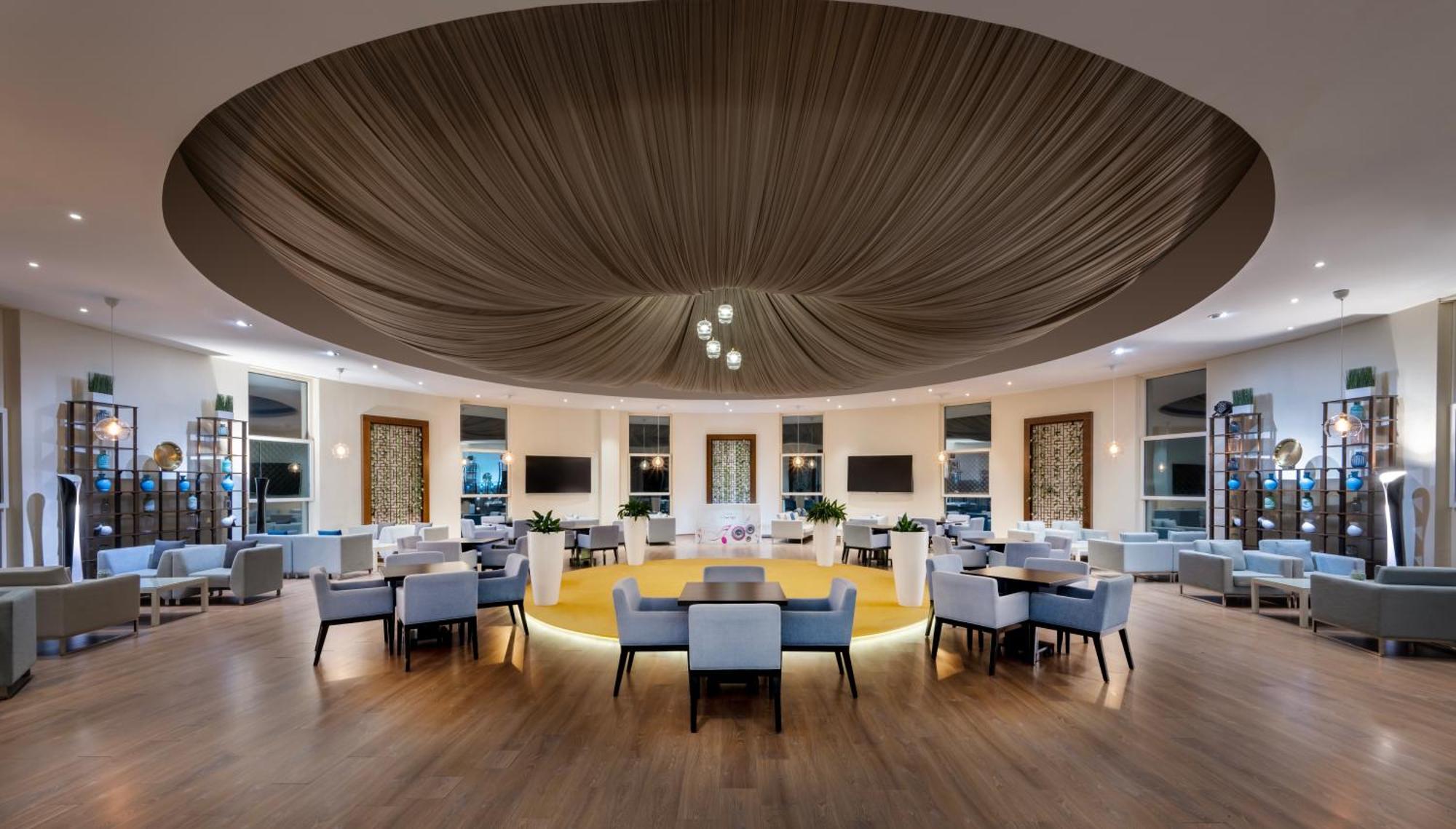 Grand Millennium Al Wahda Hotel And Executive Apartments Abu Dhabi Exterior photo The photo shows a modern and elegantly designed interior space, likely a restaurant or lounge. The ceiling features a large, draped fabric that creates a soft, ambient look. The floor is made of light wood, and there are several round and rectangular