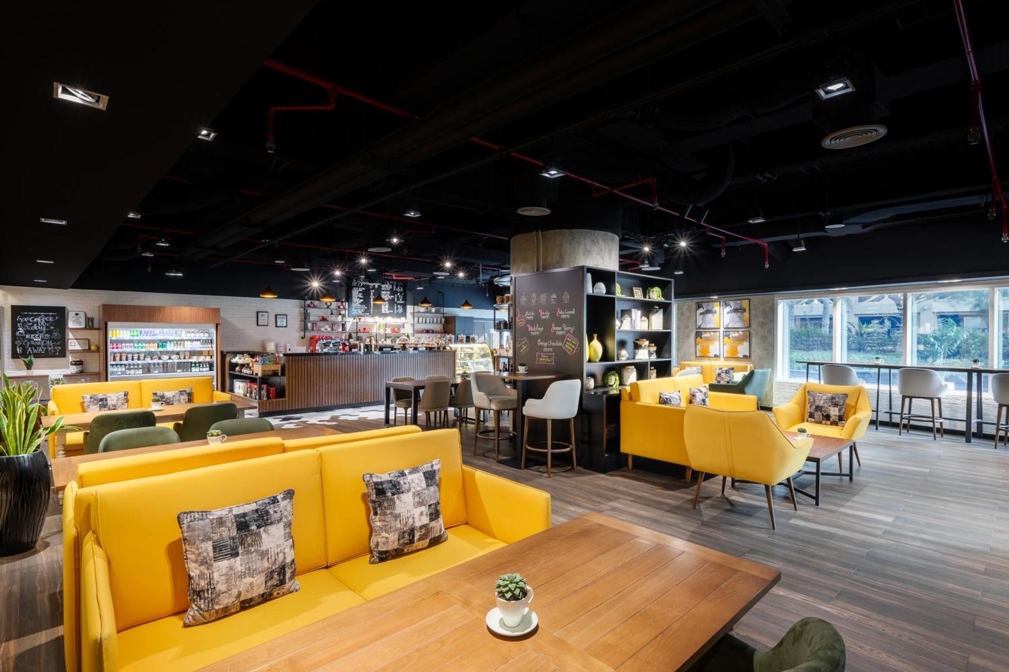 Grand Millennium Al Wahda Hotel And Executive Apartments Abu Dhabi Exterior photo The photo depicts a modern café interior. The space features a combination of seating arrangements, including yellow couches with cushions and green chairs. There are wooden tables, and the flooring appears to be a light wood. 

A bar area is visible