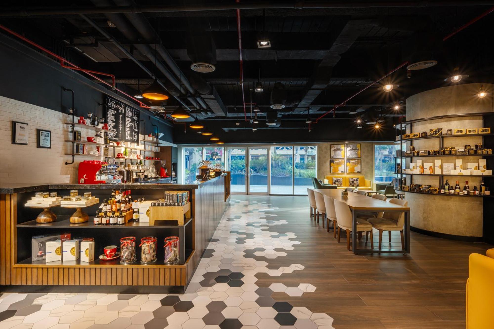 Grand Millennium Al Wahda Hotel And Executive Apartments Abu Dhabi Exterior photo The photo shows a modern and stylish café or restaurant interior. The space features a combination of wooden and tiled flooring, with a unique hexagonal pattern. On the left, there is a counter displaying various food items, likely for retail or orde