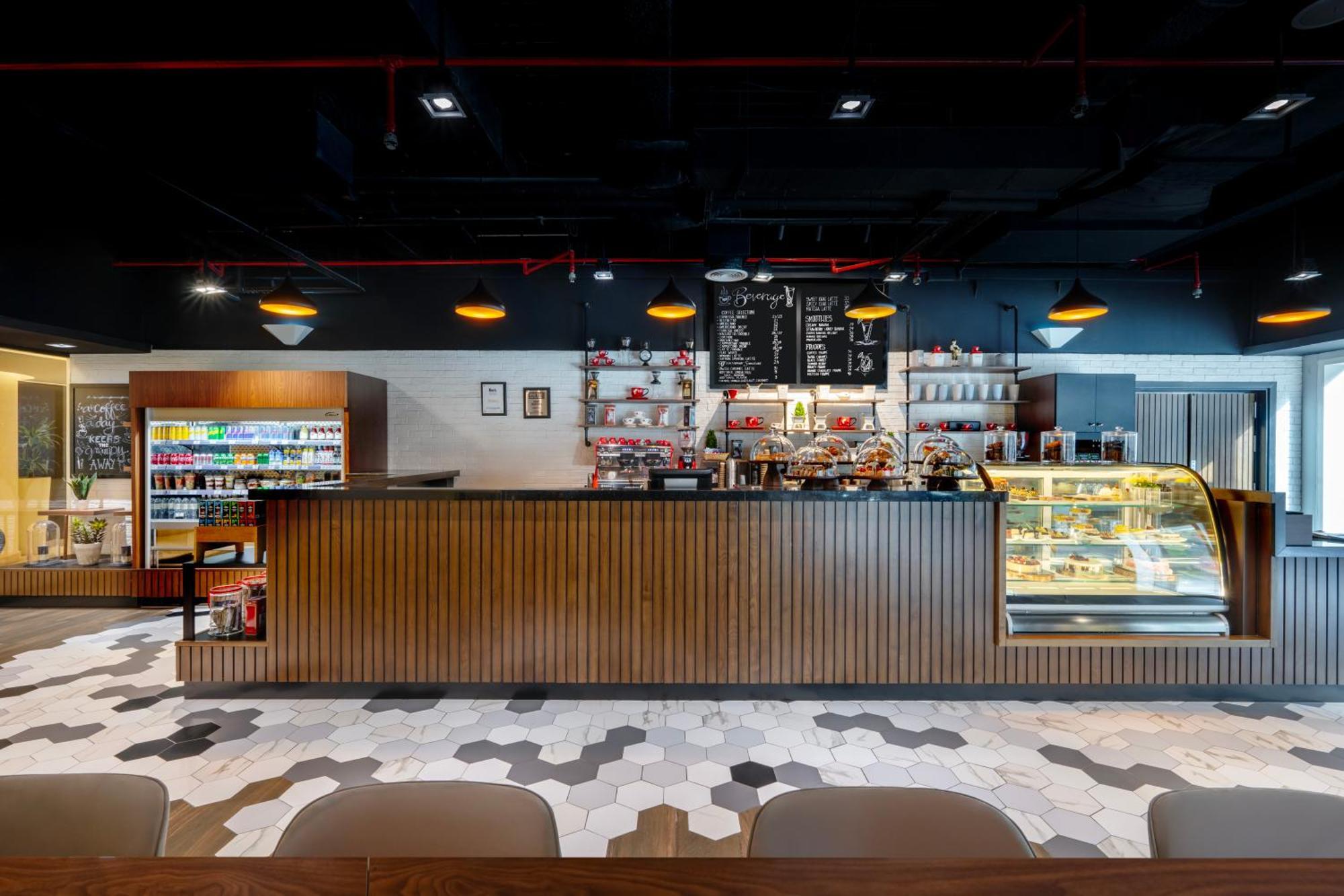 Grand Millennium Al Wahda Hotel And Executive Apartments Abu Dhabi Exterior photo The photo showcases the interior of a modern café. The focal point is a wooden counter where various beverages and pastries are likely served. Behind the counter, there is a display case with items, possibly desserts or snacks. The wall features a bl