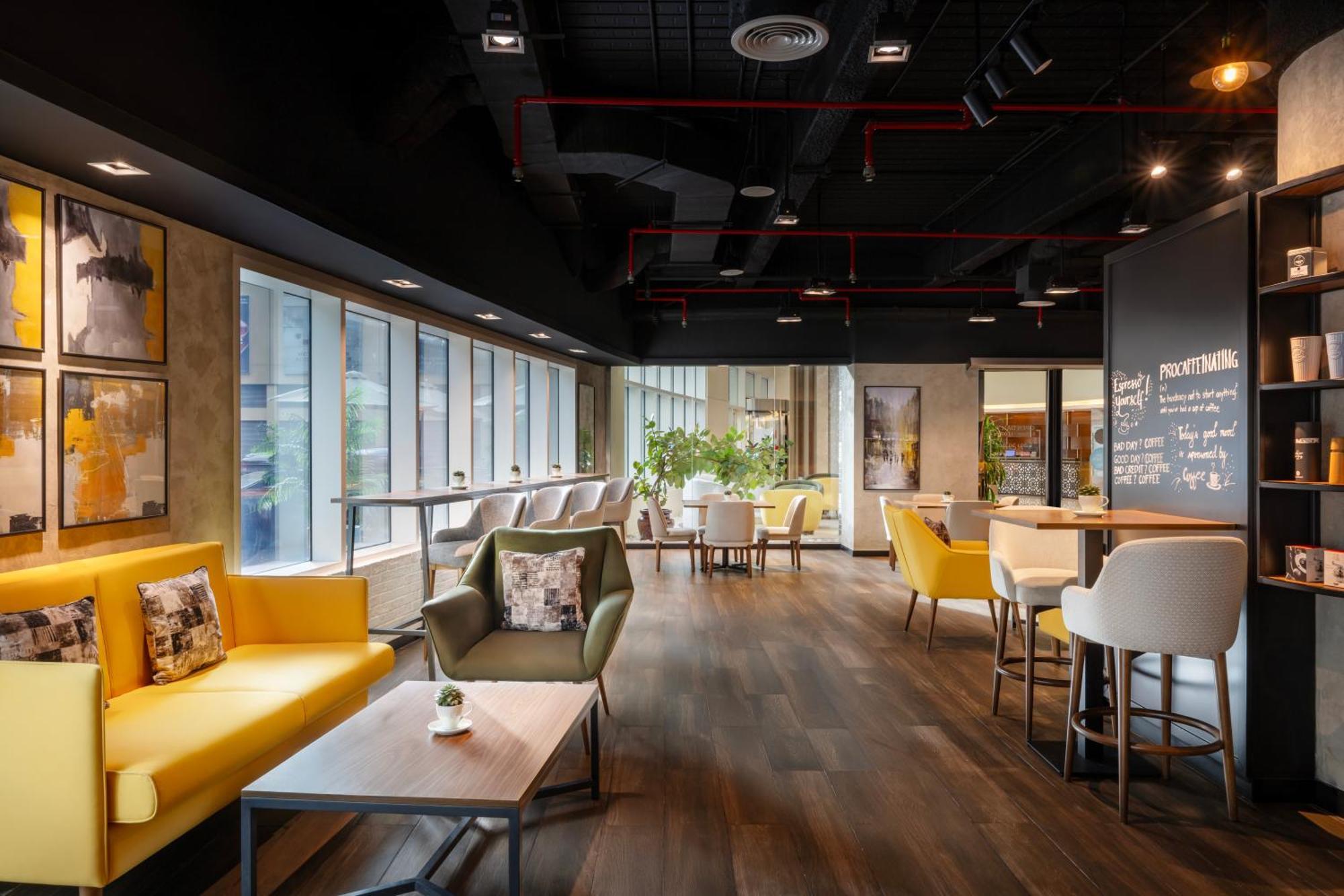 Grand Millennium Al Wahda Hotel And Executive Apartments Abu Dhabi Exterior photo The photo showcases a modern café or lounge area. There are large windows allowing natural light to fill the space. The interior features a mix of seating options, including bright yellow sofas, upholstered chairs, and wooden tables. The flooring is 